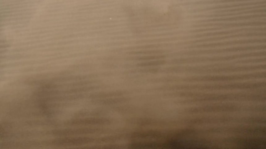 Sand explodes upwards then blows across rippled desert sand