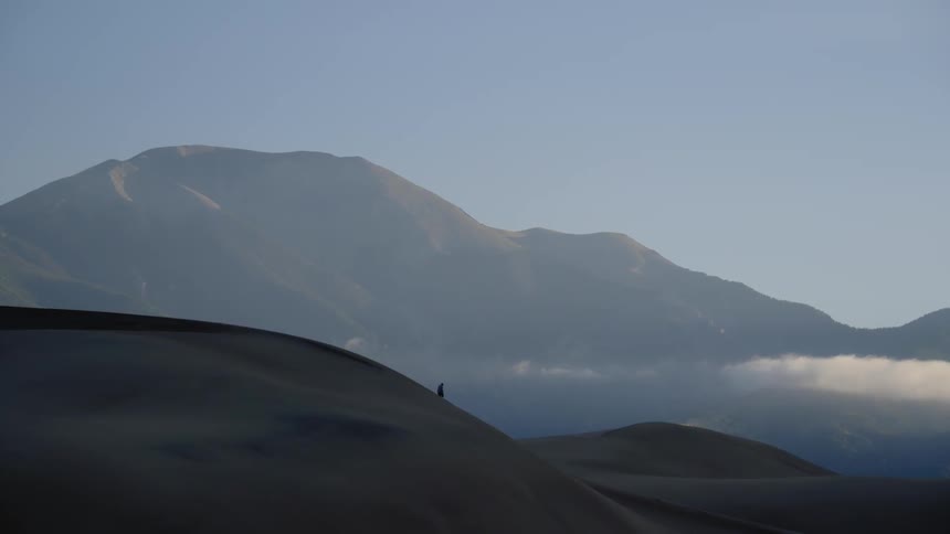 A man walks along sand dunes under a blue sky