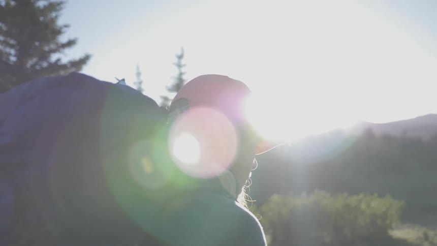 Woman wearing a pink cap and backpack walks in the forest while the sun beams