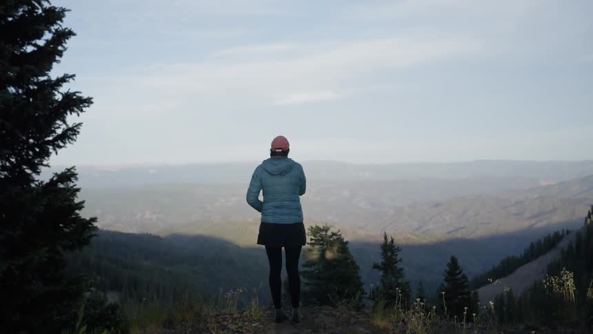 A woman with blue sweater looking through the nature scenery at the hill