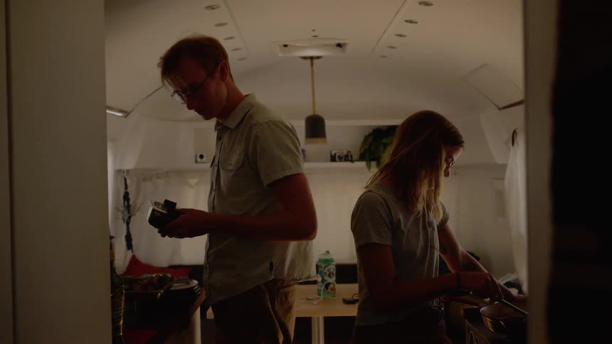 A man and woman prepare a meal while standing in the kitchen of a camper