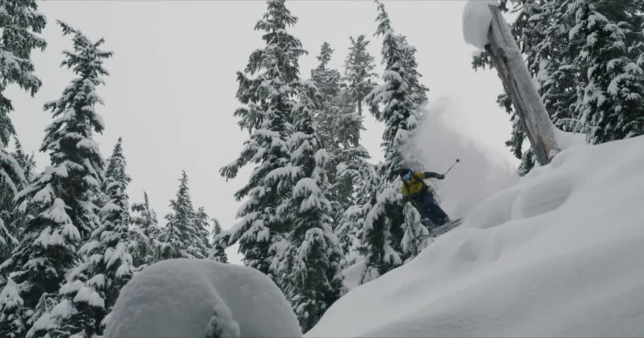 A man with yellow jacket jumping from a cliff with snow board