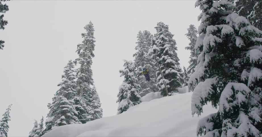 A man with yellow jacket doing downhill with a snow board