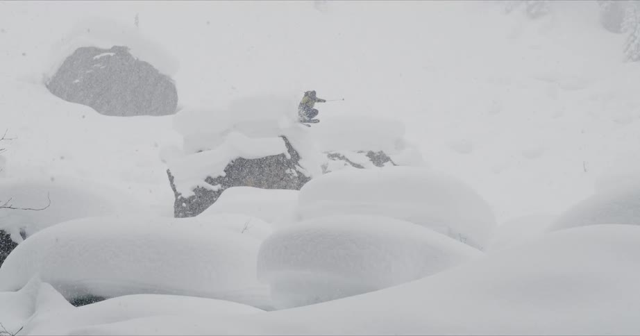 Skier jumping over snow capped rock while snowing in the back country