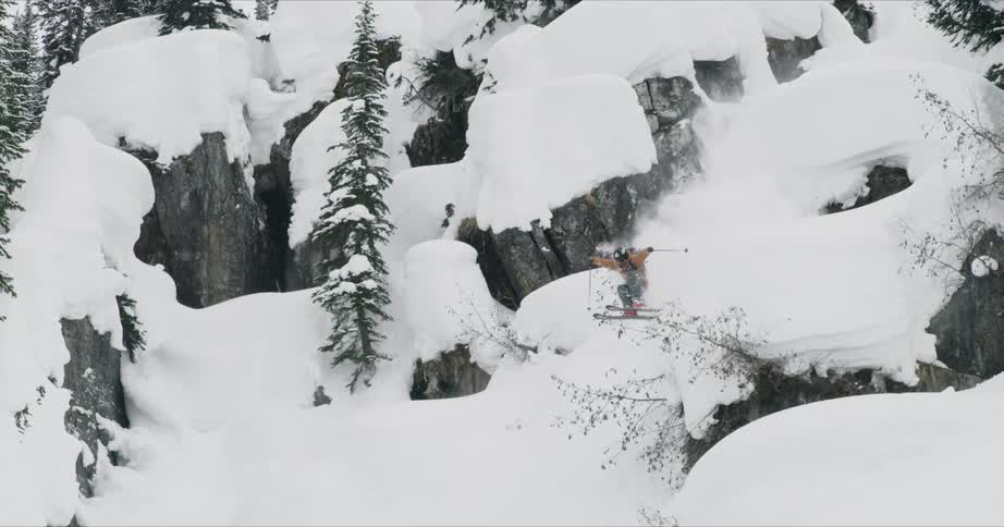 A skier jumps off the rocks and windmills his arms and poles as he lands on the slope and falls back