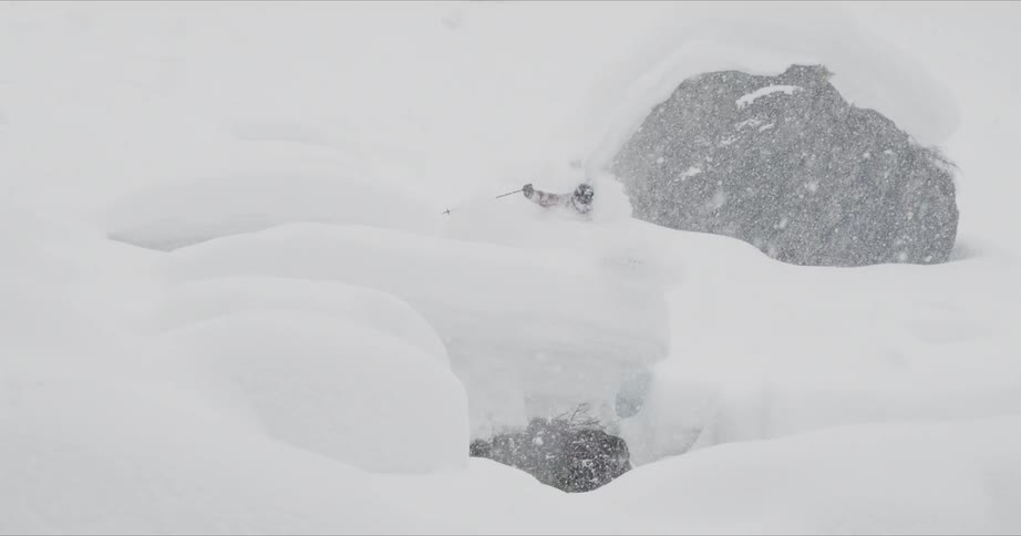A skier jumps over a mound while snow falls heavily