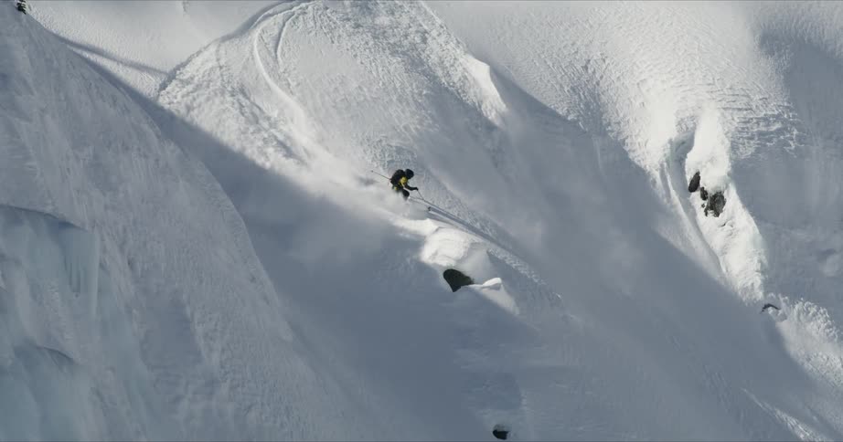 A person skis down a steep mountain in fresh snow