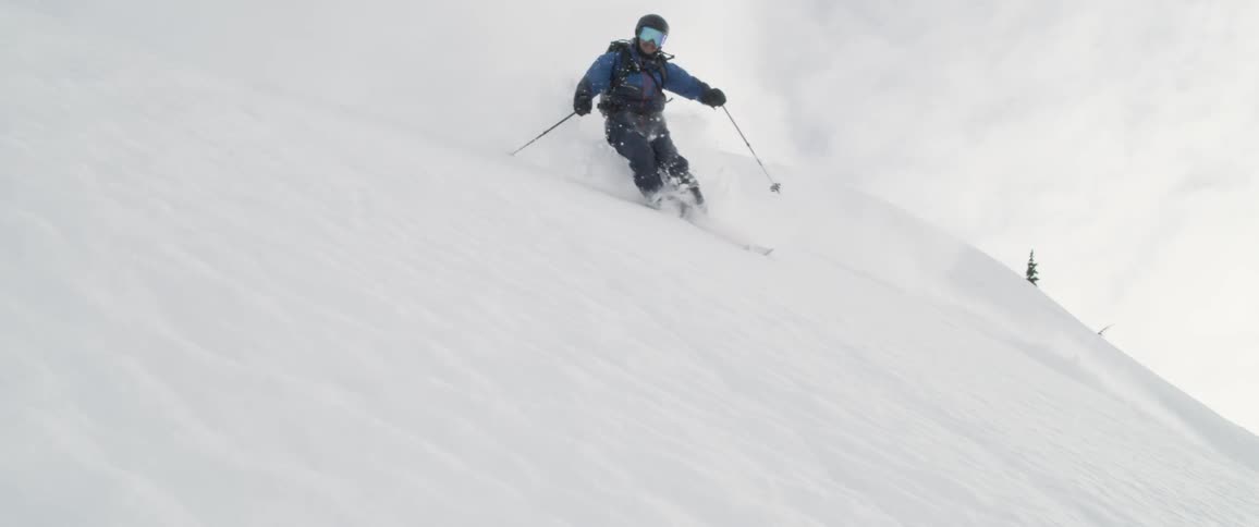Skier races down steep slope spraying snow into air
