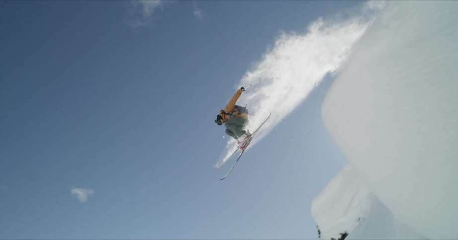 Backcountry skier jumping off a snow capped rock in the mountains