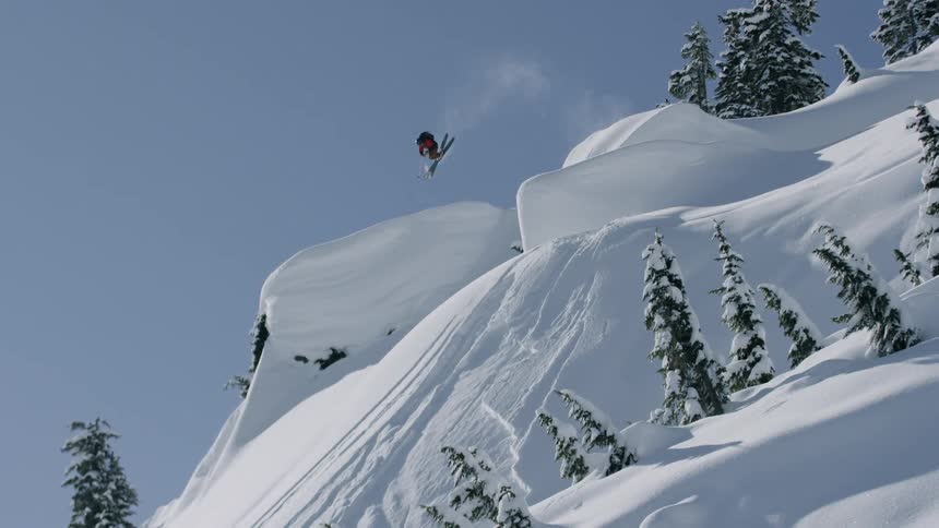 A skier leaps and twists down a steep snow covered slope