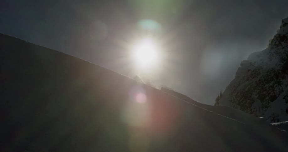 The sun shines brightly as it hangs in the sky above snow covered mountains