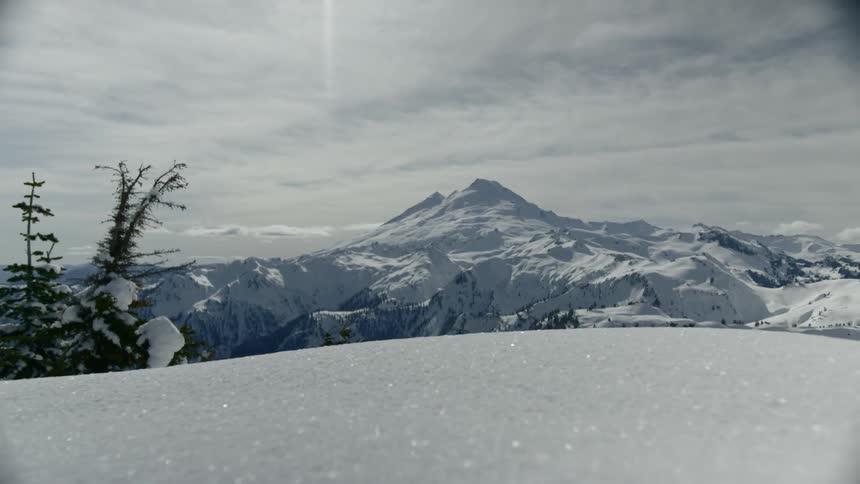 Snow covers fields and mountains under cloudy sky