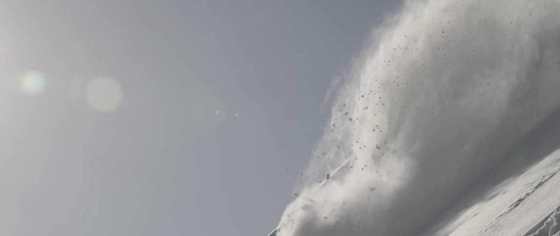 An avalanche of snow flows and blows down a mountain slope on a sunny day