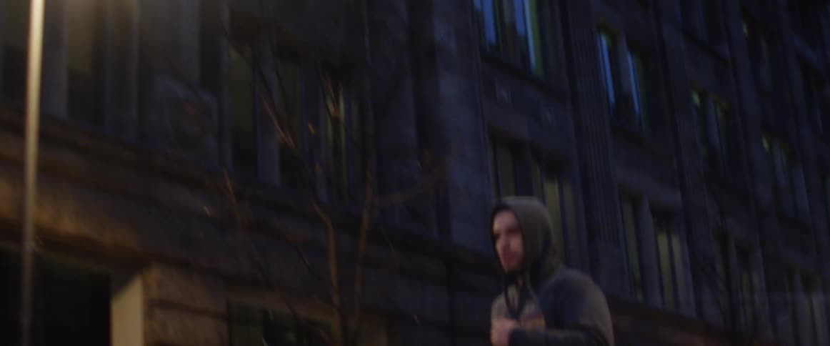 Man wearing a hoodie jogging through downtown at night