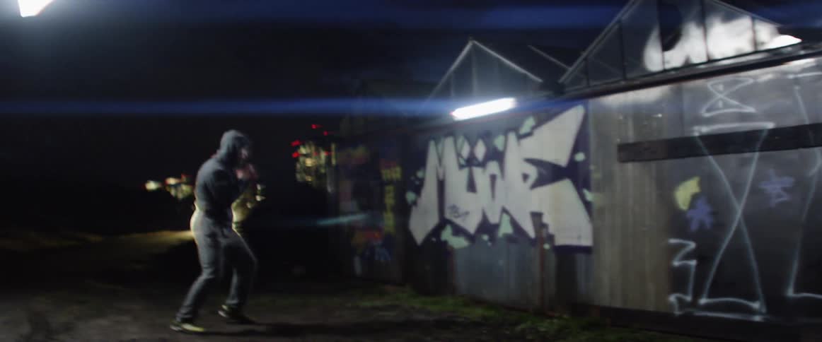 Man shadow boxes at night near graffiti covered walls