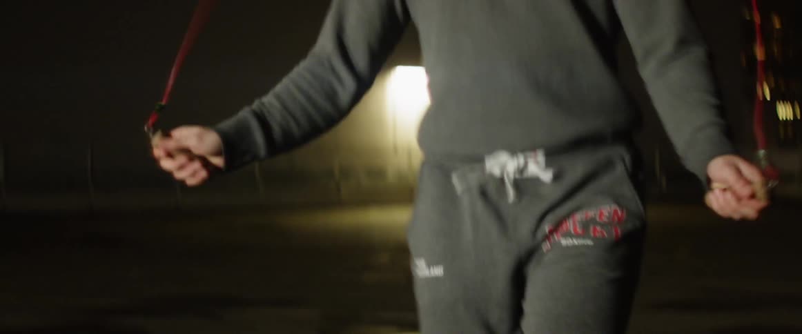 A man in sweatpants and sweatshirt jumps rope outside at night