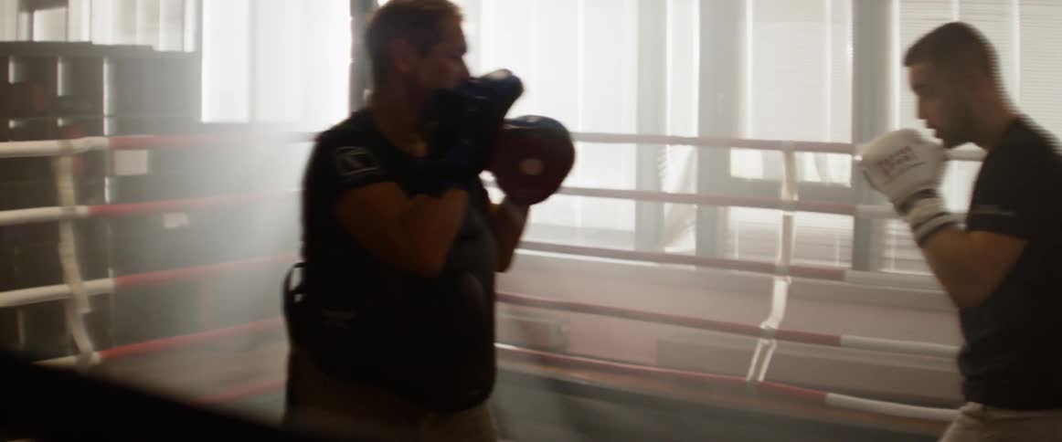 Two men boxing in a ring against the sunlight in a gym