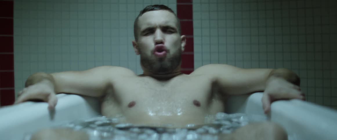 A young man grimaces and takes deep breaths as he plunges himself into a tub of icy water