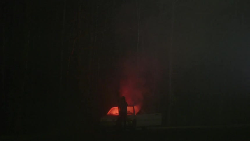 A person watches a car burn at night