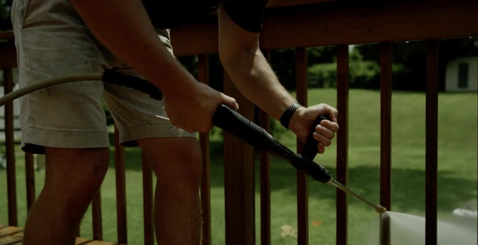 Male holds the handle of the pressure washer hoses and sprays the slats on the wooden deck in the back yard