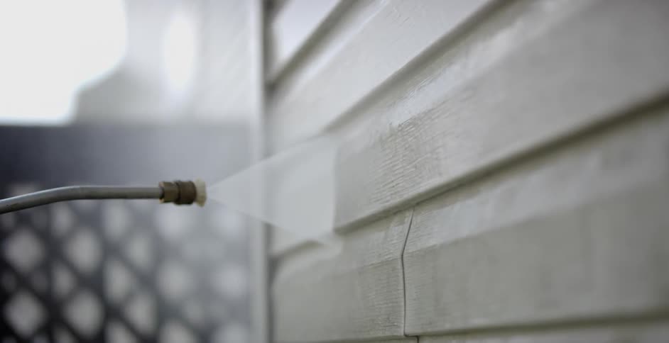 A power washer cleans dirt off the vinyl siding of a house