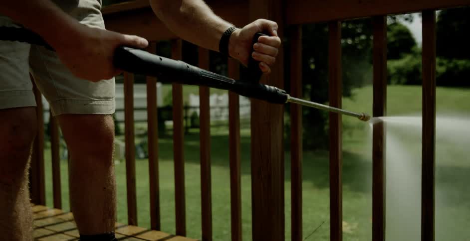 Man using power washing machine to clean up fence on porch
