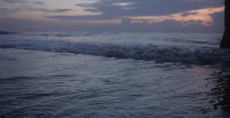 Ocean waves come to shore near the pylons of a pier at sunset