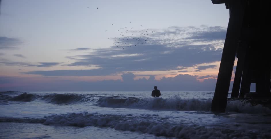 A silhouette of a man standing in the middle of the sea