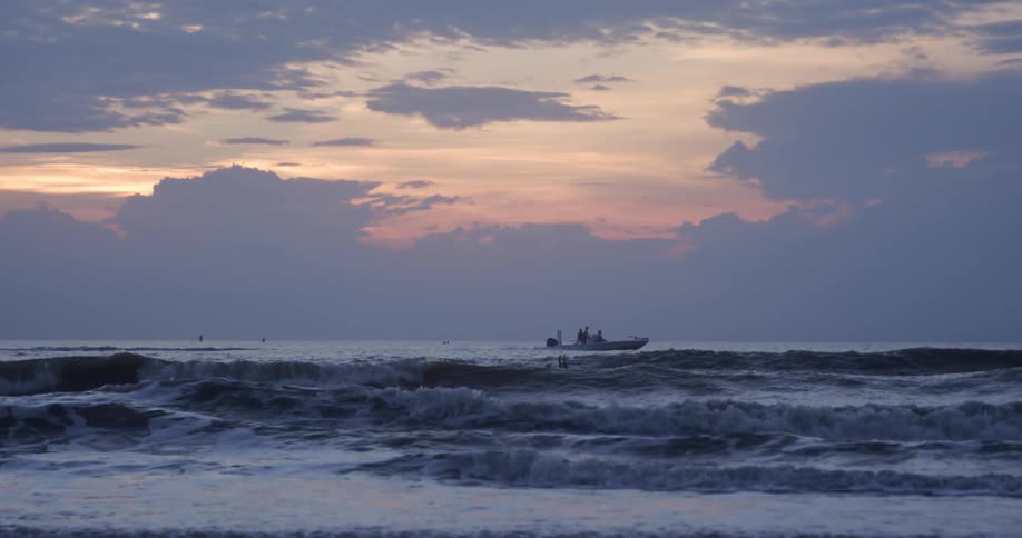 A boat passes by as a surfer paddles in the waves with legs and feet up in the air