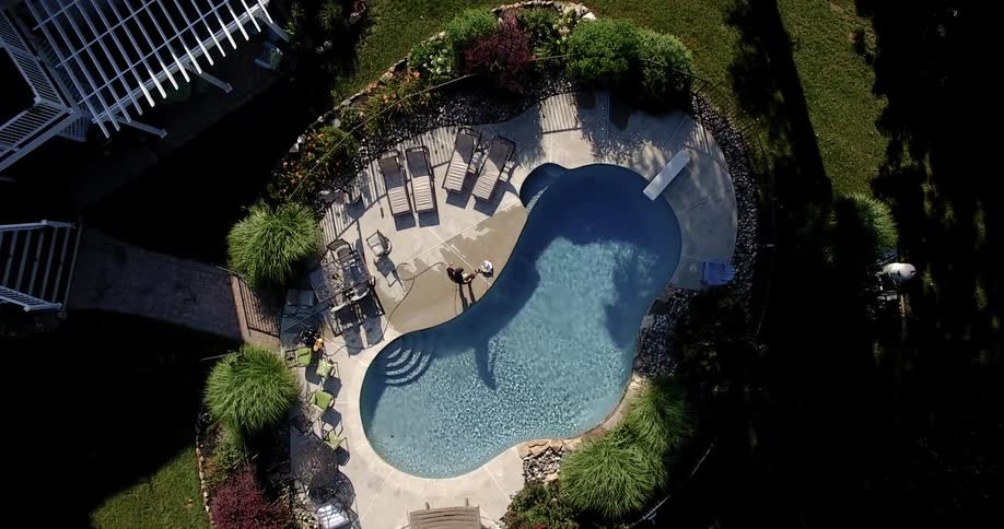 A person pressure washes the concrete deck around an in ground swimming pool in a backyard