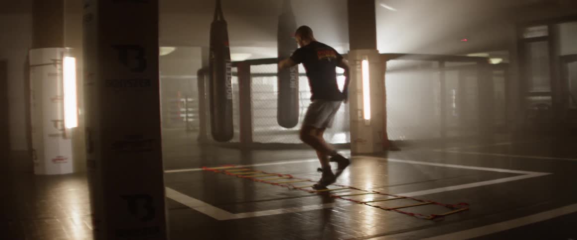 A man steps back in forth through a flat ladder on the ground training athletically