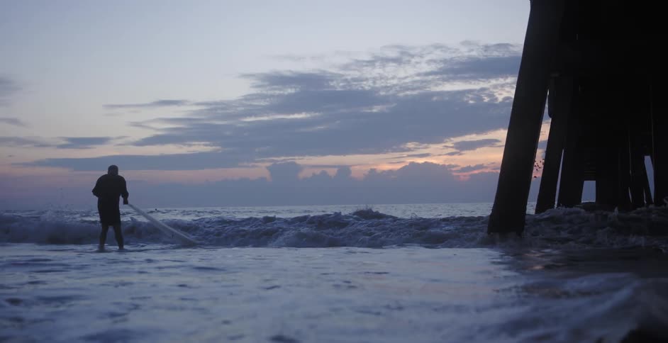 A fisherman uses a net under a pier on the ocean