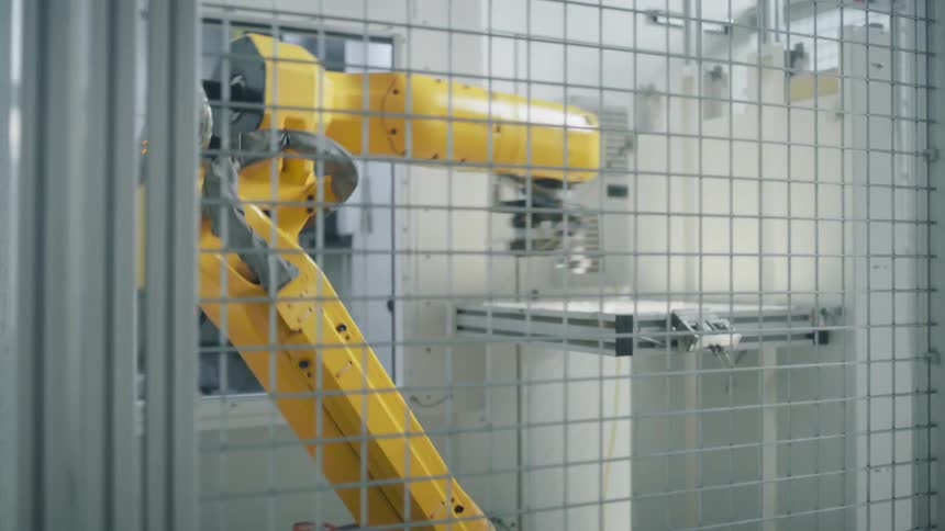 A yellow robotic arm for assembling is operating independently within a caged enclosure