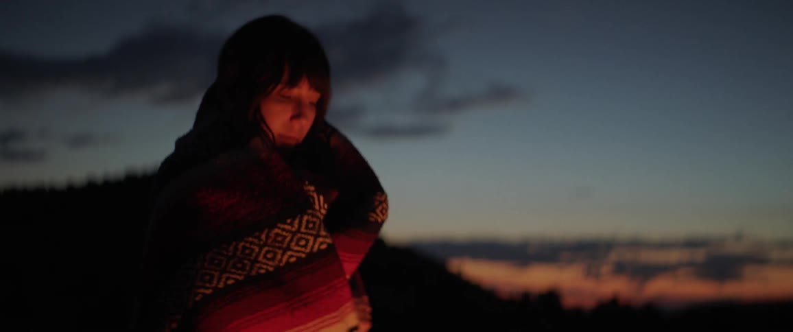 A woman wraps a blanket around her shoulders at night outside