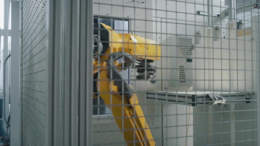 A robotic machine swings its arm through an opening while working in a metal cage