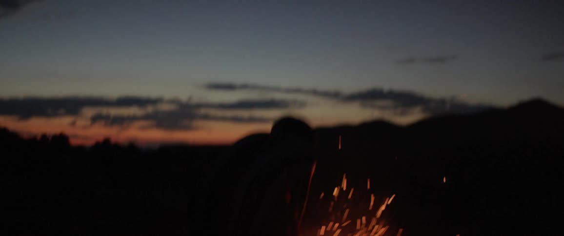 A person is jumping around a fire outdoors at dusk