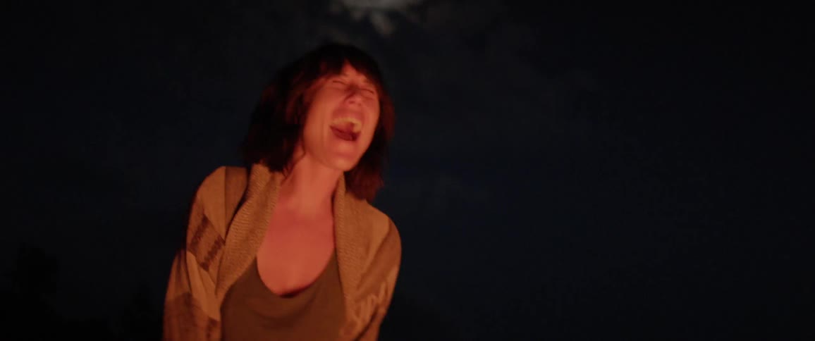 A woman screaming in front of a campfire at night