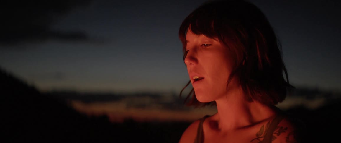 A woman with tattoos on her shoulder rests by a fire at night