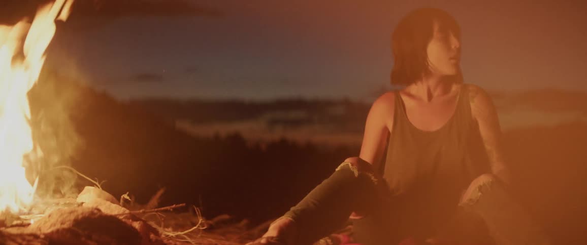 A brunette white woman sits by a campfire and heaves a big sigh