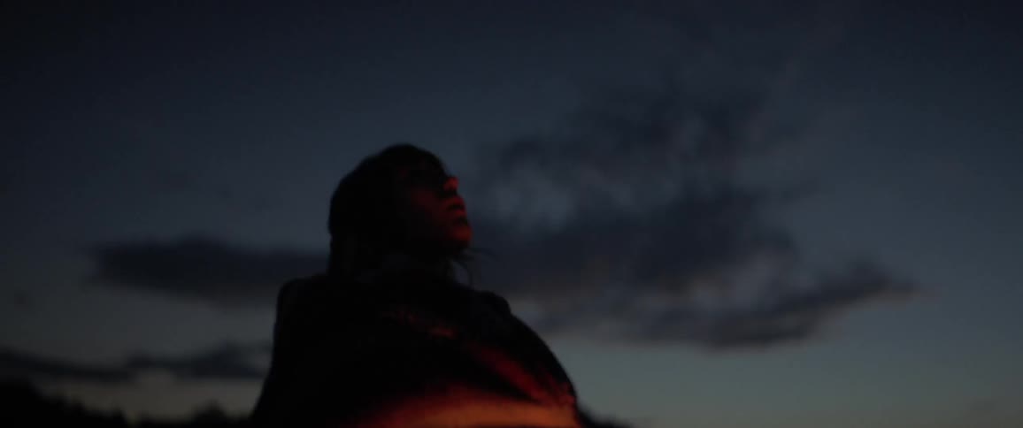 A young woman looks up at the night sky and wraps a blanket around herself