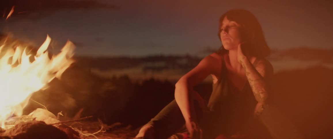 A tattooed woman sitting next to a campfire at night