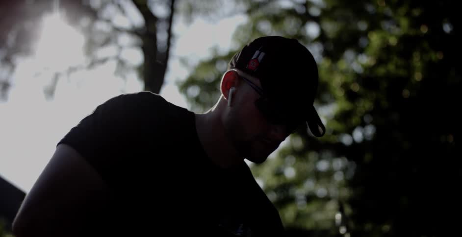 A man in a baseball cap bends over as he stands in front of a tree