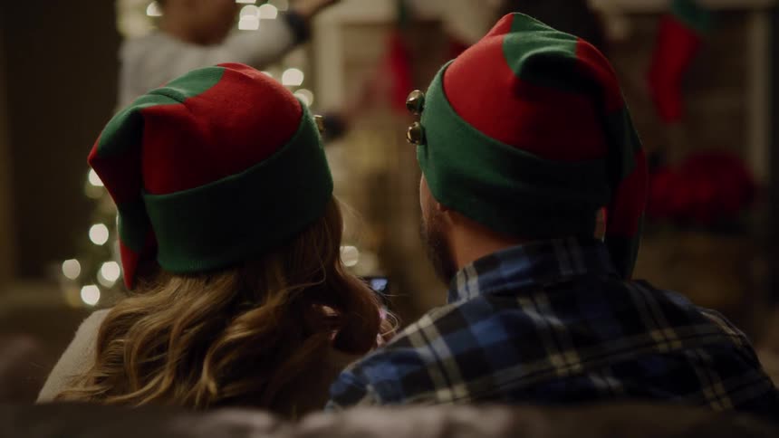 A man and woman watch their children play next to a christmas tree with white lights