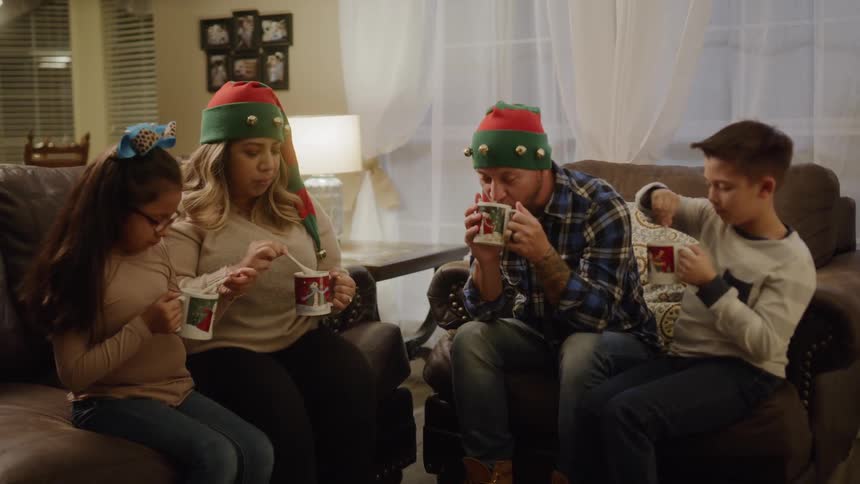 A family in festive hats drink something from holiday mugs