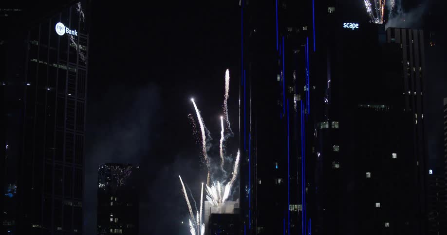 Fireworks up above a city block with many tall skyscrapers at night