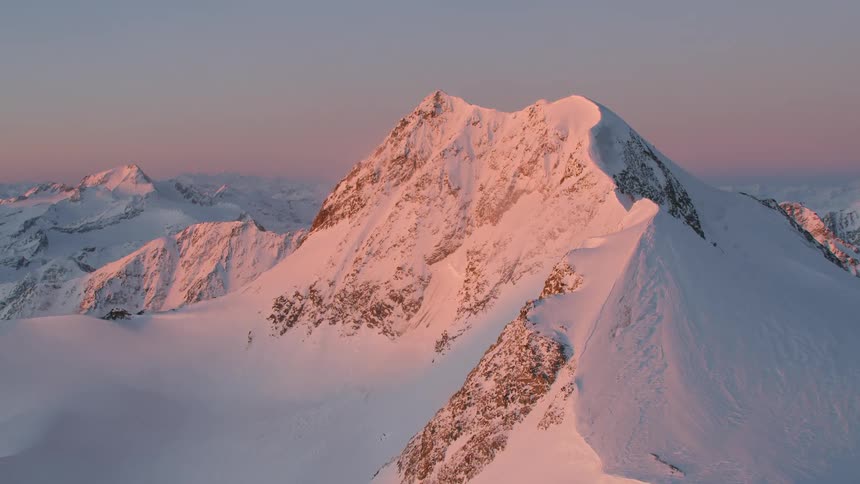 An aerial footage of a snowy mountain peak on the dawn