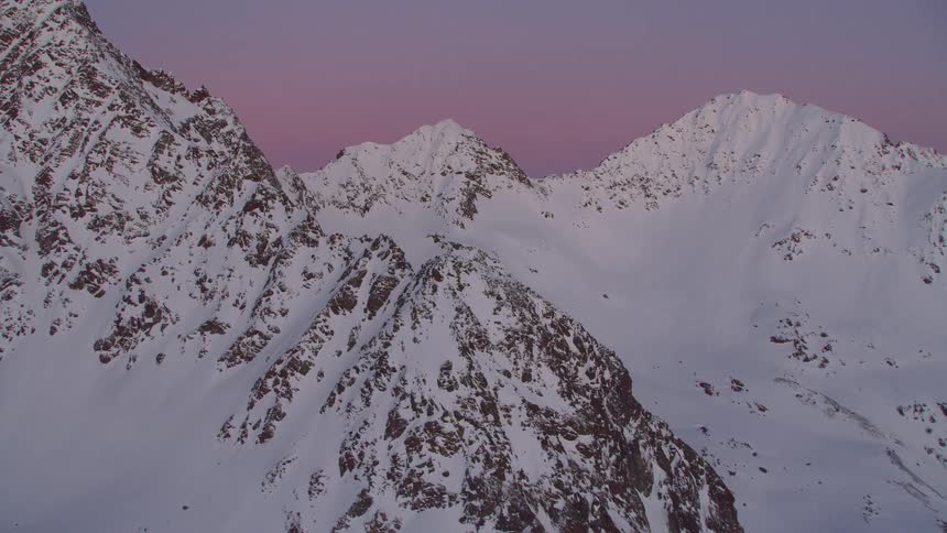 An aerial footage of an icy mountain peak with red sky background