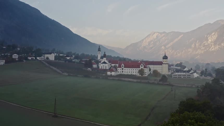 A large estate with towers and a church surrounded by mountains