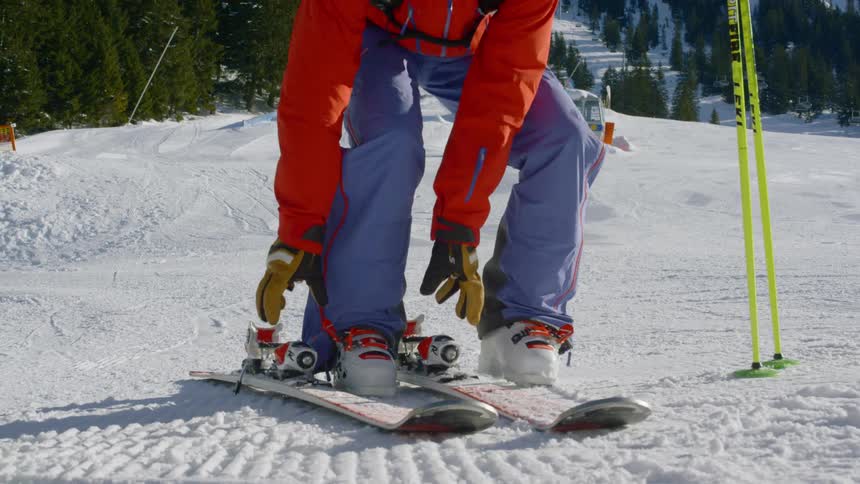 A woman removes her skis at the bottom of a snow hill