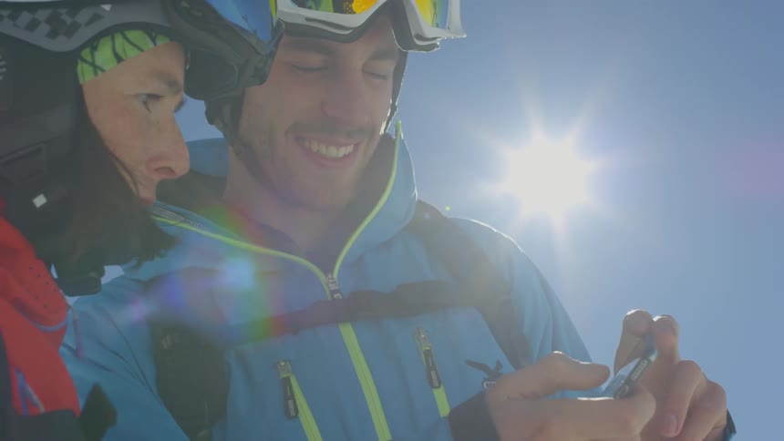 A man wearing ski gear shows his girlfriend also wearing ski gear something on his phone
